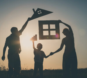Happy family standing on the field at the sunset time. They build a house. Concept of friendly family.